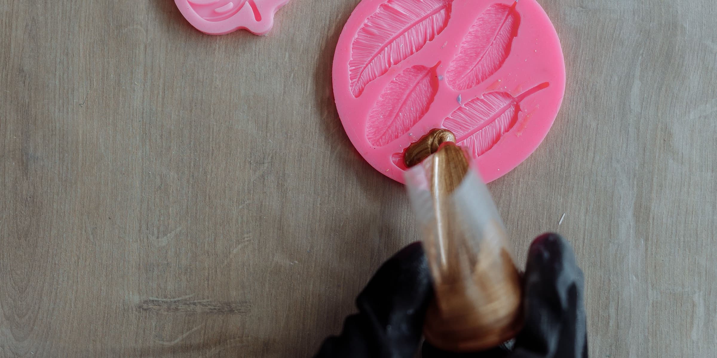 Gloved hand pouring resin into pink silicone moulds